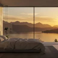 Modern luxury bedroom with floor-to-ceiling windows overlooking North Idaho mountain lake at golden hour sunrise, representing premium lakefront living opportunities now more accessible with Federal Reserve rate cuts